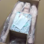 Multifunctional patient care manikin for nursing training with IV injection arm, catheterization module, and airway management kit in packaging box.