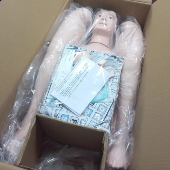 Multifunctional patient care manikin for nursing training with IV injection arm, catheterization module, and airway management kit in packaging box.